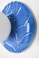 Close-up of Lierre ceramic sconce in Sky Blue celadon-style glaze, glossy botanical ivy leaf texture with color pooling in the relief, matte white globe diffuser, modern organic lighting for hallway, bathroom, or bedroom