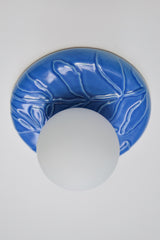 Front view of Lierre ceramic wall sconce or ceiling fixture in Sky Blue celadon glaze, round 7.5 inch leaf relief plate with matte white globe shade, minimal studio product photo on white background