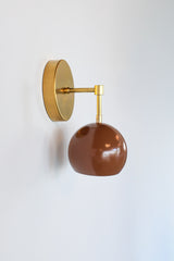 A chocolate brown dome on a brass arm, and it looks great against a pale wall. The Loa Sconce has a round brass backplate, a short arm that turns down at a brass elbow and a glossy Fudge brown shade that hangs open-side down. The warm brown and natural brass sit well together. It’s a good fit beside a bed, over a reading chair or in a hallway where you want a light with some depth.