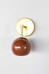 A chocolate brown dome on a brass arm, and it looks great against a pale wall. The Loa Sconce has a round brass backplate, a short arm that turns down at a brass elbow and a glossy Fudge brown shade that hangs open-side down. The warm brown and natural brass sit well together. It’s a good fit beside a bed, over a reading chair or in a hallway where you want a light with some depth.