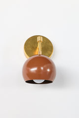 A chocolate brown dome on a brass arm, and it looks great against a pale wall. The Loa Sconce has a round brass backplate, a short arm that turns down at a brass elbow and a glossy Fudge brown shade that hangs open-side down. The warm brown and natural brass sit well together. It’s a good fit beside a bed, over a reading chair or in a hallway where you want a light with some depth.