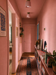 Long blush pink hallway painted wall to trim, with a matching pink door, vintage runner rug, framed art, bookshelves, and a hanging plant for a collected, maximalist feel. A pair of blush pink Marcella flushmounts with brass hardware repeat down the ceiling, adding soft decorative lighting to the narrow corridor. The ribbed ceramic shades bring a playful Art Deco, grandmillennial, and dopamine decor look, perfect for pink hallway lighting, small space ceiling lights, colorful cottage interiors, and quirky s