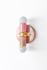 Angled side profile of a blush pink marbled Thalia wall sconce with creamy swirls and gold veining, photographed to emphasize its rounded backplate and dimensional shape. The brass hardware adds warmth and a more elevated, “designer” finish, while the globe bulb keeps it classic and simple. This sconce works beautifully in vanity lighting moments, small-space lighting, colorful bathrooms, and playful modern bedrooms. Ideal for anyone searching pastel lighting, feminine-but-not-frilly decor, eclectic wall sc