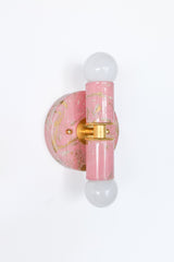 Three-quarter side view of the blush pink, cream, and gold marbled Thalia sconce, highlighting the glossy marbled surface and the way the color wraps around the backplate and center column. The compact scale makes it easy to use as a pop of color in a powder room, a kids’ bathroom that still feels sophisticated, or a tucked-away reading nook. Brass accents and globe bulb styling keep it grounded in a modern, mid-century-leaning look. Great for searches like colorful wall sconces, small bathroom lighting, do