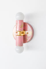 Side-angle view of the hand-marbled Thalia sconce in blush pink, cream, and gold, showing the fixture’s depth and sculptural profile. The round backplate, brass collar detail, and vertical center column create a clean, architectural silhouette, while the marbled finish adds a one-of-a-kind, painterly look. This compact wall light is a perfect choice for bathrooms and powder rooms, especially beside a mirror or in a tight hallway where you want a small statement piece. A great fit for dopamine decor, eclecti