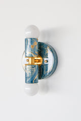 Close-up of the Thalia Sconce in lagoon, cream, and gold marbled finish, showing glossy swirled color, brass center band, and white globe bulbs. Compact two-light wall sconce or flush mount ceiling light with an art-object look, perfect for high-impact accent lighting in powder rooms, hallways, and modern eclectic spaces.