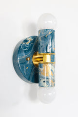Lagoon, cream, and gold marbled Thalia Sconce installed vertically as a two-light wall sconce with brass accents and white globe bulbs. Compact statement lighting with glossy marbled color, great for bedside lighting, powder rooms, and hallways in modern eclectic interiors.