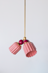 A fuller view of the Marcella Small Chandelier in pastel pink and black cherry, hanging on its full brass rod to show scale and drop length. The glossy pink shades and rich burgundy balls pair together for a romantic, feminine look with real presence, good for picturing placement over a nursery dresser or a bedroom reading nook.