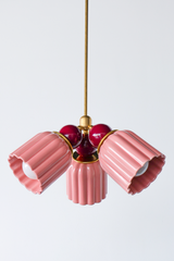 A bottom-up look at the Marcella Small Chandelier in pastel pink and black cherry, with all three glossy fluted shades fanned out symmetrically around the brass center and burgundy connector balls. This angle shows the full silhouette clearly, a romantic, grandmillennial-leaning pick for a bedroom or nursery that wants softness with some real color depth.