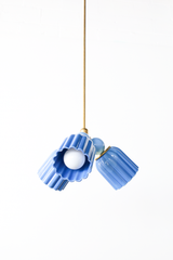 A straight-on look at the Marcella Small Chandelier in sky blue and hydrangea blue, its fluted cone shades fanned outward from a central brass fitting on a slim brass rod. This angle shows the full hang length and the relationship between the two blue tones clearly, useful for picturing scale and proportion before placing it over a breakfast nook table or in a nursery.