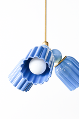 A close crop on two of the Marcella Small Chandelier’s fluted cone shades, one lit from inside to show off the scalloped, almost flower-like edge. The deep periwinkle blue shade color pairs with a lighter hydrangea blue glass ball just visible behind it. A good reference shot for seeing the exact texture and shape of the shade before deciding on this fixture for a nursery or breakfast nook.
