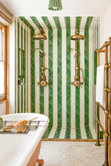 Bright, spa-like bathroom featuring our Marcella Flushmount in a glossy jade green ceramic shade with warm brass hardware, mounted above a bold green-and-white striped tile shower surround. This airy, design-forward space mixes vintage-inspired brass plumbing, a freestanding tub, and clean white walls for a fresh take on classic coastal and grandmillennial style. Great search terms: green bathroom ceiling light, jade green flush mount, brass flushmount ceiling fixture, ceramic flush mount lighting, art deco