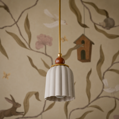 A cream-colored ceramic shade with vertical ribbing hangs beneath a mahogany-toned sphere finial, grounded by warm brass hardware. The matte cream glaze reads soft and approachable against botanical wallpaper featuring birds and delicate branches in earth tones. The mahogany finial—deep and warm—adds a subtle richness without overwhelming the gentle palette.