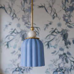 A periwinkle ceramic shade hangs from a brass rod, topped with a glossy white sphere finial. Vertical ribbing catches light across the glazed surface. The shade reads soft and romantic—almost whisper-quiet in tone—against delicate botanical wallpaper. The brass accents bring warmth to the cool blue-violet, creating an unexpectedly sophisticated pairing.This pendant feels collected and curated—like something found in a vintage French bathroom or a literary character's thoughtfully designed powder room. 