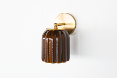 A closer look at the construction behind this handmade pottery sconce: a brass arm meets a ball finial and ring collar before the art deco fluted shade begins, its celadon-style glaze pooling rich chocolate brown down every groove. Small-batch, one-of-a-kind, and built to bring feminine, jewel-toned warmth to a colorful bathroom or serve as ambient lighting in a larger room.