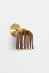 The Marcella Sconce hangs its fluted bell shade downward in a rich amber Chicory Brown, the glaze streaking naturally across each rib for a warm, handmade look. A brass ball finial and ring collar connect it to a full round backplate. A grounded, moody choice for warm traditional bathrooms, hallways, and bedrooms that want lighting with real depth of color.