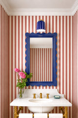 A bold, preppy powder room moment featuring our Marcella Sconce in glossy cobalt blue with warm brass hardware, mounted above a scalloped mirror on red and white striped wallpaper. This look is perfect for anyone searching for a blue ceramic wall sconce, cobalt blue bathroom sconce, statement powder room lighting, coastal inspired bathroom design, or grandmillennial bathroom decor. The saturated blue shade pops against the classic stripe, while the brass faucet and marble sink keep it polished and timeless 