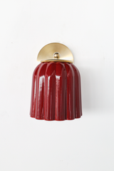 Head-on, the Marcella Sconce shows its fan-shaped brass backplate sitting above a ball finial and ring collar, which hold the fluted jasper red shade in place. The deep, mottled red glaze and clean brass geometry make this a statement piece for colorful traditional bathrooms, hallways, and bedrooms looking for lighting with real depth of color.