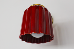 This angle shows how the Marcella Sconce projects off the wall: a brass arm extends from a round backplate, ending in a ball finial and ring collar that cradle the fluted jasper red shade. The downward-facing bell shape means the glow washes softly rather than glaring, ideal for powder rooms and moody hallways that want saturated color with a soft touch.