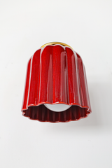 This angle shows how the Marcella Sconce projects off the wall: a brass arm extends from a round backplate, ending in a ball finial and ring collar that cradle the fluted jasper red shade. The downward-facing bell shape means the glow washes softly rather than glaring, ideal for powder rooms and moody hallways that want saturated color with a soft touch.