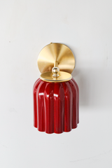The Marcella Sconce hangs its fluted bell shade downward in a deep, mottled jasper red that reads almost like glazed ceramic. A brass ball finial and ring collar connect it to a full round brass backplate, giving the whole fixture real weight and presence. A moody, saturated choice for colorful traditional bathrooms, hallways, and bedrooms that want lighting with texture and depth.