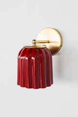 Seen in profile, the Marcella Sconce shows off its silhouette: a brass arm curves gently down from a round backplate to the fluted jasper red shade, finished with a brass ball and ring collar. The downward bell shape and rich, mottled red make this a striking pick for moody powder rooms, hallways, and colorful traditional bedrooms.