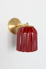 Seen in profile, the Marcella Sconce shows off its silhouette: a brass arm curves gently down from a round backplate to the fluted jasper red shade, finished with a brass ball and ring collar. The downward bell shape and rich, mottled red make this a striking pick for moody powder rooms, hallways, and colorful traditional bedrooms.