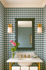 Grandmillennial powder room with green gingham wallpaper, a scalloped black mirror, and a matching pair of Marcella ceramic wall sconces in cream unglazed porcelain with brass backplates. Marble countertop and undermount sink with a vintage-inspired brass faucet, plus fresh pink flowers and crisp white towels. Great inspiration for bathroom vanity lighting, traditional bathroom decor, preppy powder room style, and modern classic interiors.