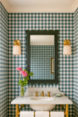 Traditional powder room with Southern charm featuring green gingham wallpaper, cream ceramic Marcella wall sconces with brass backplates, a scalloped black mirror, and a classic white marble vanity with brass fixtures. The fluted sconces and playful patterns give the space a timeless yet updated feel, perfect for a preppy, coastal-inspired home in Nantucket or a refined Southern cottage.