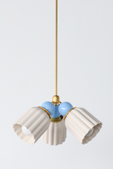A small chandelier with matte, fluted ceramic cone shades in unglazed cream, paired with glossy celestial blue powder-coated steel balls and brass hardware. The soft, light palette makes this a strong fit for a nursery, a coastal-leaning bedroom, or a gentle grandmillennial space that wants delicate color without heavy contrast. Shown hanging on its full brass rod, giving a sense of scale and drop length.