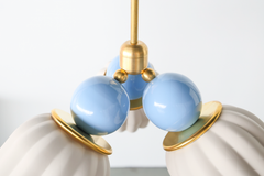 A wider close-up of the Marcella Small Chandelier in unglazed cream and celestial blue, showing three of the matte fluted ceramic shades meeting at the brass center fitting with the glossy blue connector balls on full display. The soft, light palette makes this a strong fit for a nursery, a coastal-leaning bedroom, or a gentle grandmillennial space that wants delicate color without heavy contrast.