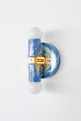 Close-up view of the Mediterranean Blue, Cream & Gold marbled Thalia sconce, featuring a round backplate and cylindrical center in a high-gloss marbled pattern. The brass hardware adds a warm pop against the cool blue tones.