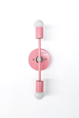 Straight-on product photo of blush pink Medium Thalia wall sconce with chrome hardware, vertical double-bulb modern wall light with round backplate and frosted globe bulbs, clean lined mid century modern vanity sconce for bathrooms, powder rooms, bedrooms, and design-forward contemporary interiors