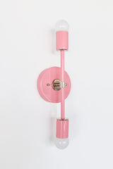 Blush pink Medium Thalia wall sconce with chrome hardware, sleek modern mid century style vertical double sconce with round backplate and two frosted globe bulbs, designer wall lighting for bathroom vanity lighting, bedside sconces, entryway, hallway, and modern minimalist or colorful contemporary homes
