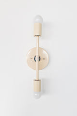 Front view detail of the Medium Thalia wall sconce in cream with chrome hardware, featuring two exposed globe bulbs at top and bottom and a clean linear stem over a round backplate, modern minimalist wall lighting for bathrooms, bedrooms, hallways, and design forward homes