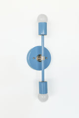 Angled product photo of the Medium Thalia Sconce in Hydrangea blue with chrome hardware and white globe bulbs. This slim two-light sconce adds soft color without feeling overwhelming, making it a sweet choice for colorful bathrooms, children’s bathrooms, powder rooms, bedrooms, and playful grandmillennial spaces.