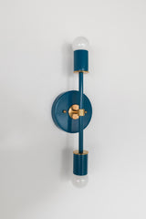 Side-angle studio image of the Lagoon Medium Thalia Sconce, shown on a clean white wall with brass hardware and white globe bulbs. The saturated blue-green finish gives this fixture a colorful but polished look, perfect for bathroom vanity lights, kids bathrooms, coastal-inspired rooms, powder rooms, bedrooms, and other spaces where decorative wall lighting needs to feel both fun and refined.