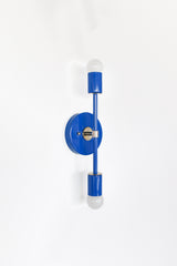 Angled product photo of the Mediterranean Blue and chrome Medium Thalia Sconce, a vertical double-globe wall light with a bright blue finish, round wall plate, slim center rod, and polished chrome accents. The clean linear shape makes it a great colorful sconce for bathroom mirrors, powder room lighting, hallway walls, bedside lighting, kids spaces, and modern eclectic interiors that need a pop of blue.