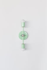 Mint green Medium Thalia wall sconce with chrome hardware, shown straight-on as a vertical double light fixture with globe bulbs at top and bottom. Glossy mint powder-coated backplate and cylindrical sockets create a clean modern silhouette ideal for bathroom vanity lighting, hallway sconces, bedroom wall lights, kids room lighting, and colorful maximalist interiors.