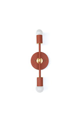 Terra Cotta and brass Medium Thalia Sconce photographed from below in a horizontal position, showing the round wall plate, straight bar, warm clay-orange finish, brass center detail, and globe bulbs at each end. This two-light wall sconce has a clean geometric shape that feels modern, vintage-inspired, and a little mid century, making it a great option for bathroom vanity lighting, colorful powder rooms, eclectic hallways, or bedrooms that need a small but bold wall light.