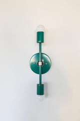 Front-facing studio photo of the Medium Thalia Sconce in glossy Mermaid Green with polished chrome hardware and two white globe bulbs. This colorful vertical wall sconce has a clean modern shape with a retro feel, making it a great fit for bathroom vanity lighting, powder rooms, kids bathrooms, hallways, bedrooms, and interiors that mix bold color with crisp chrome accents.
