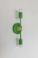 Side-angle studio image of the Medium Thalia Sconce in a vivid Spring Green finish with brass hardware and white globe bulbs. The glossy green powder-coated fixture adds a fresh, happy note to bathroom lighting, hallway lighting, children’s rooms, powder rooms, and colorful interiors inspired by playful modern, grandmillennial, or retro design.