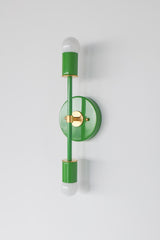 Angled product photo of the Medium Thalia Sconce in Spring Green with brass accent hardware, shown on a clean white wall. The slim two-light design brings color without feeling bulky, making it a great choice for bathroom mirrors, small powder rooms, kids spaces, modern bathrooms, and eclectic interiors with colorful lighting.