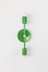 Front-facing studio photo of the Medium Thalia Sconce in a bright Spring Green finish with chrome hardware and two white globe bulbs. This colorful vertical wall sconce has a clean modern shape that works well for bathroom vanity lighting, kids bathrooms, playful powder rooms, hallways, bedrooms, and cheerful interiors that need a polished pop of green.