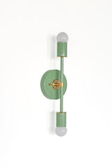 Angled view of the Medium Thalia sconce in vista green with brass accents, featuring a slim vertical silhouette and double bulb design, a sculptural mid century modern wall light for powder rooms, hallways, and eclectic interiors.