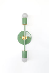 Modern mid century wall sconce in vista green powder coated steel with warm brass hardware and two exposed globe bulbs, a tall vertical statement light for bathrooms, bedrooms, and wallpapered spaces that want a pop of color.