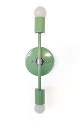 Front view of the Medium Thalia wall sconce in vista green with chrome accents and two exposed bulbs, a modern mid century inspired vertical light fixture that adds color and sculptural style to powder rooms, entryways, and bedside walls.