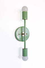 Tall mid century modern wall sconce in vista green powder coated steel with polished chrome accents and two exposed globe bulbs, a sleek vertical statement light for bathrooms, hallways, bedrooms, and colorful wallpapered spaces.