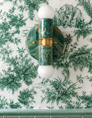 Close-up of a Mermaid Green, cream, and gold hand-marbled Small Thalia Sconce mounted vertically on green jungle toile wallpaper with animal and botanical details. The petite two-bulb wall sconce has a custom, handmade marbled finish that works beautifully in green bathrooms, colorful powder rooms, kids bath spaces, chinoiserie decor, grandmillennial rooms, and layered maximalist interiors.