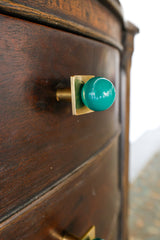 Close-up of a Mermaid Green and brass Square Gumball knob installed on a vintage wooden dresser. Glossy green powder-coated ball sits on a raw brass square base, adding bold, colorful style to antique furniture. Ideal for modern cabinet hardware, drawer pulls, and custom home accents.